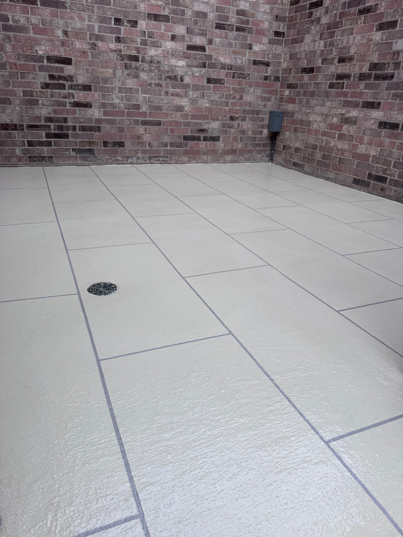A tiled floor with a drain against a brick wall.
