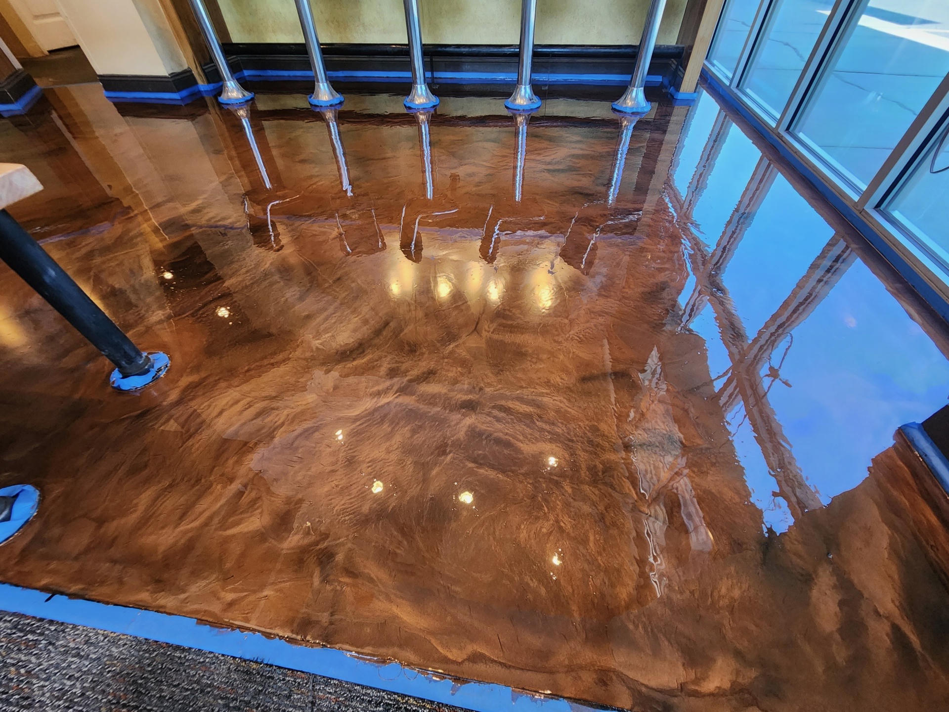 Shiny, polished epoxy floor with a rich brown finish reflecting lights and windows.